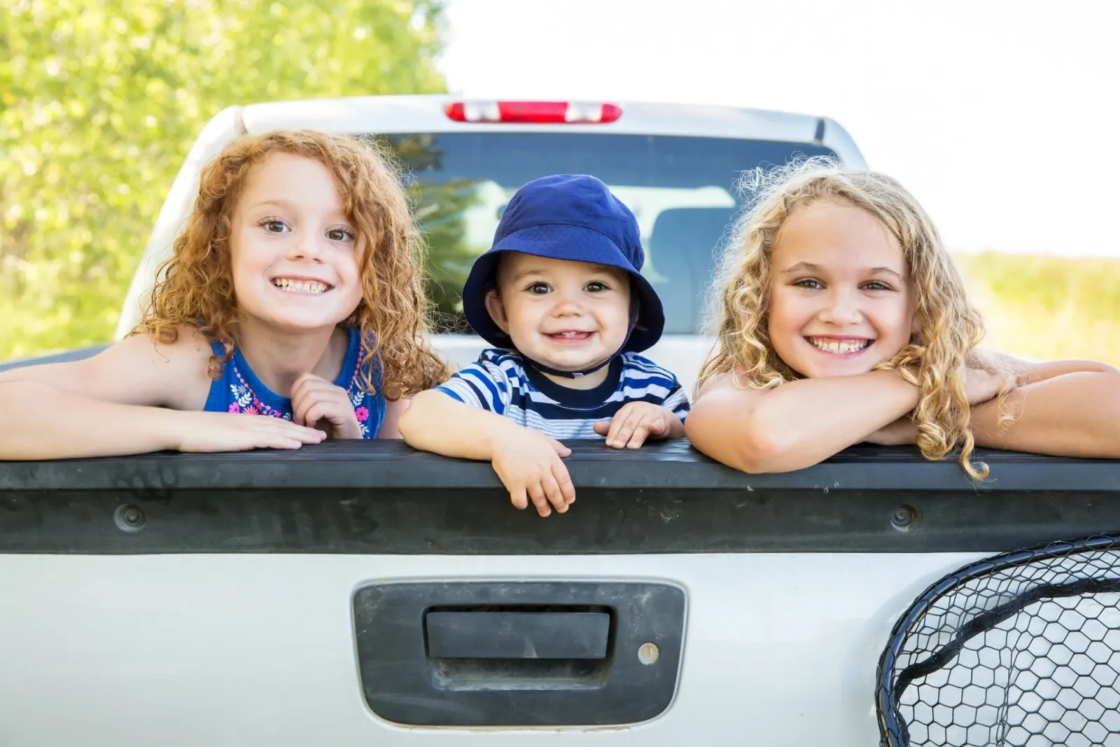 Three smiling children leaning over the tailgate of a pickup truck